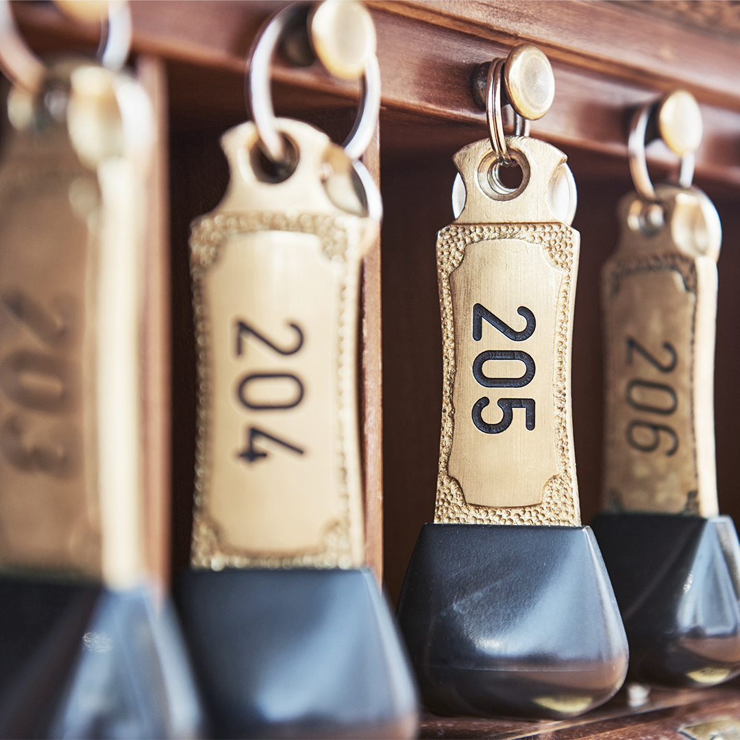 Image of brass hotel room keys on a wooden rack, showing room numbers 203-207.  Useful for hotel or hospitality marketing.