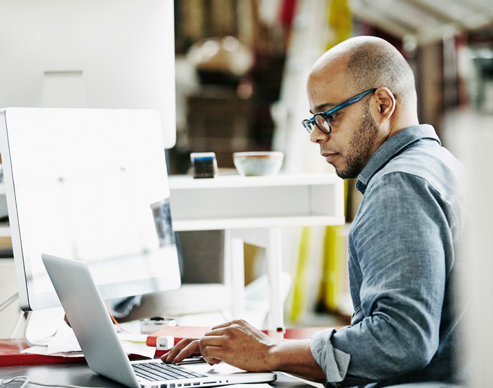 Professional working at a computer workstation with laptop and monitor