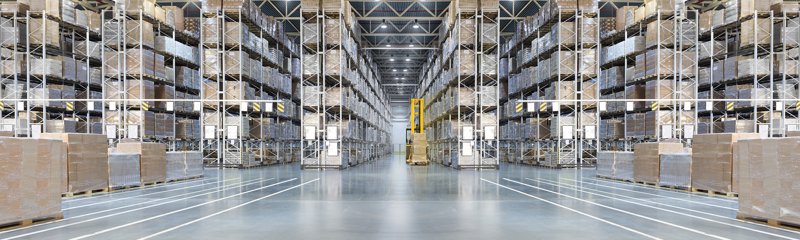 Large warehouse with tall shelves filled with stacked pallets and a forklift in the center aisle.