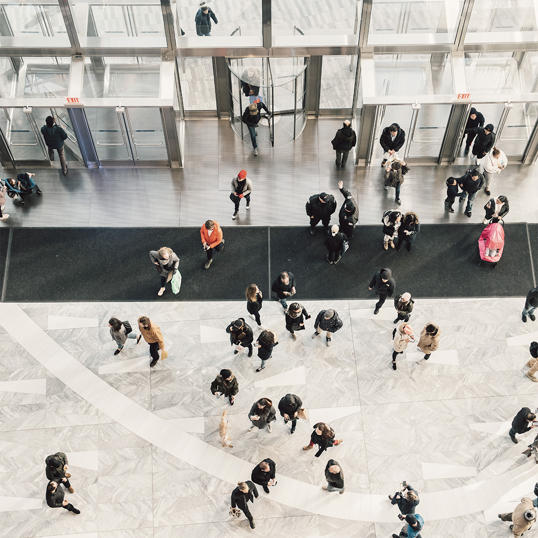 Aerial view of people walking through building lobby with glass doors and marble floors