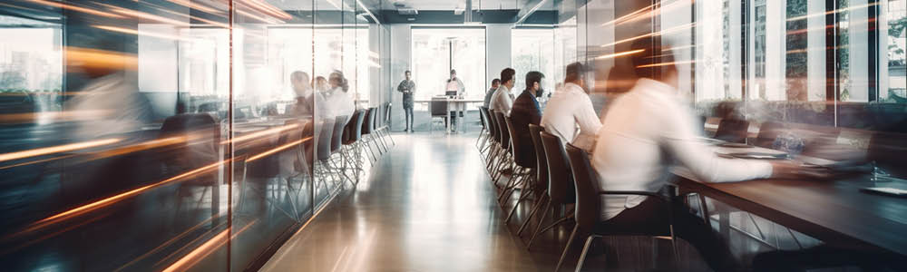 Modern office space showing a group of business professionals working collaboratively at a long table in a bright, contemporary setting.