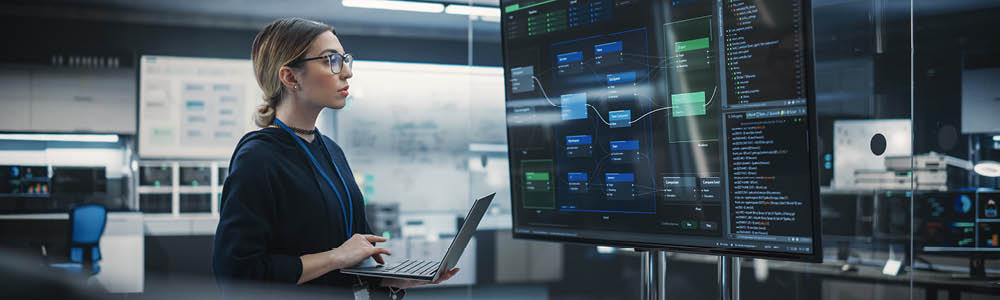Woman reviewing data on a large monitor and laptop
