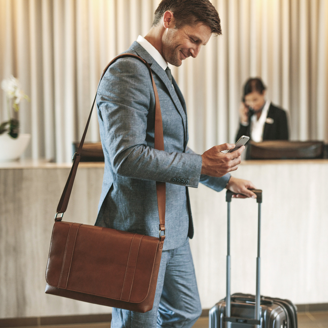 Businessman using his phone while checking into a hotel with his luggage.