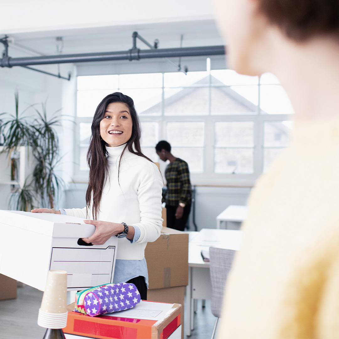 Smiling woman moving boxes in an office setting during a relocation.