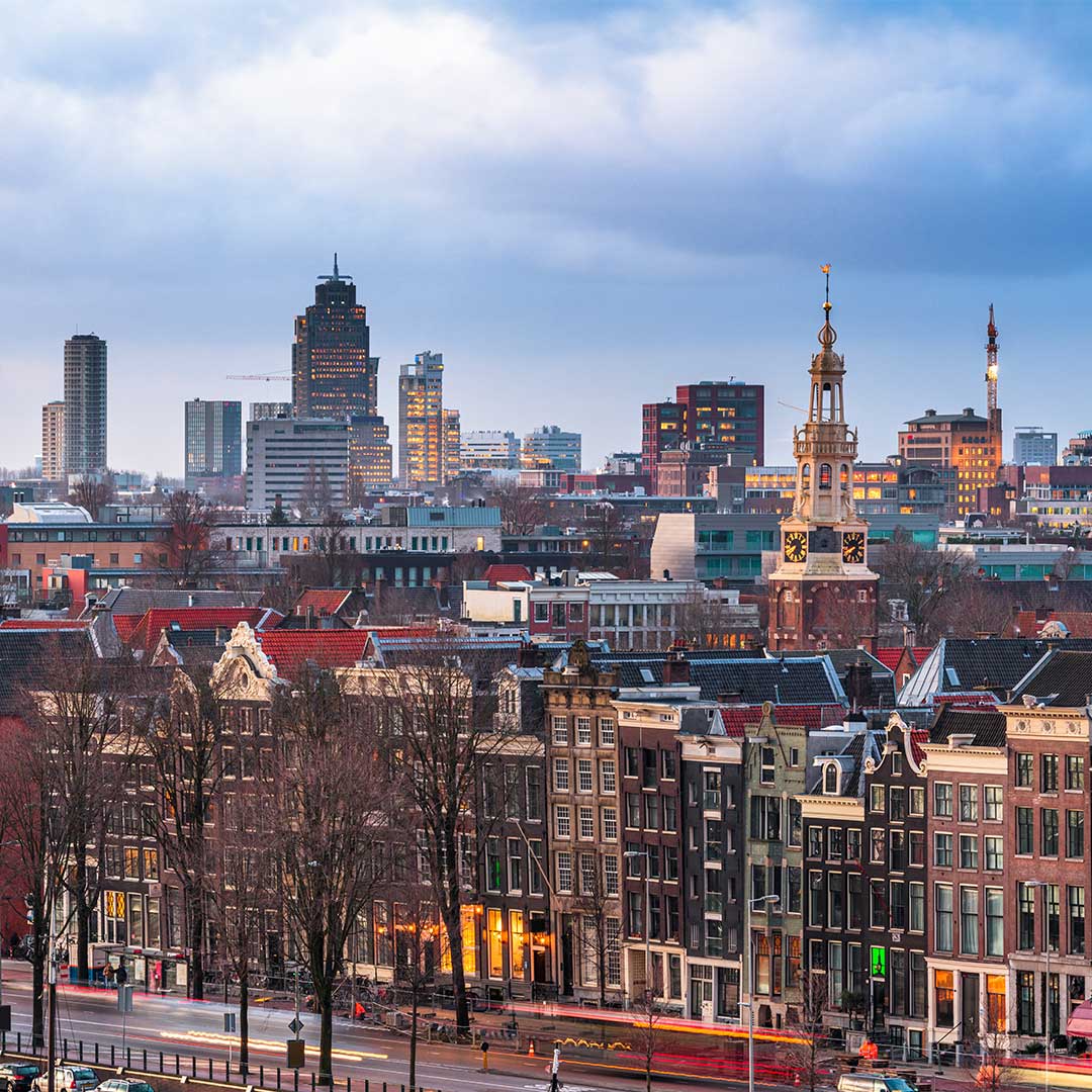 The image is a panoramic view of Amsterdam, Netherlands, at dusk or dawn.