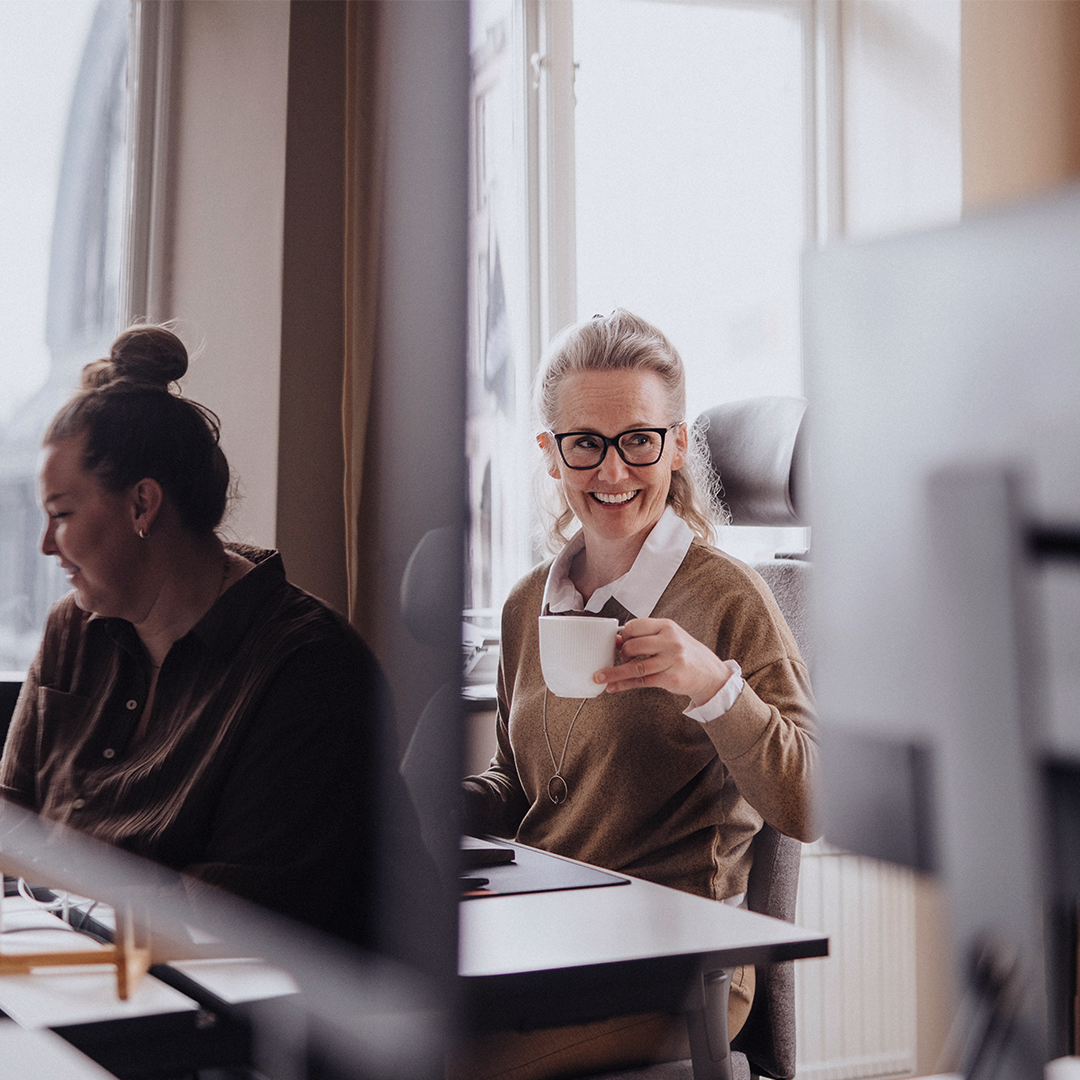 Employee smiling and drinking coffee in office