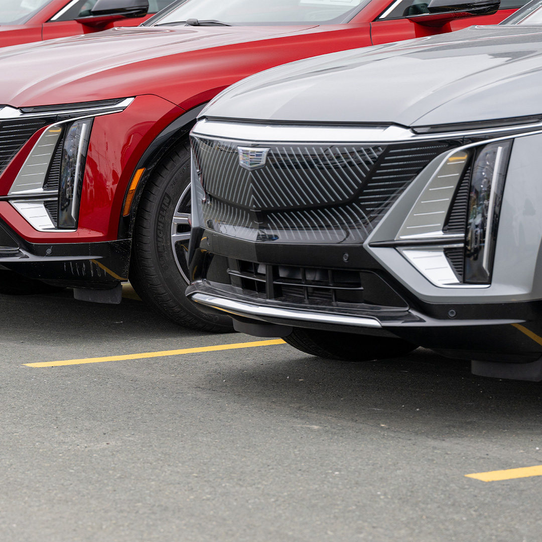 Front grilles and headlights of red and silver Cadillac Lyriq luxury electric vehicles parked side by side