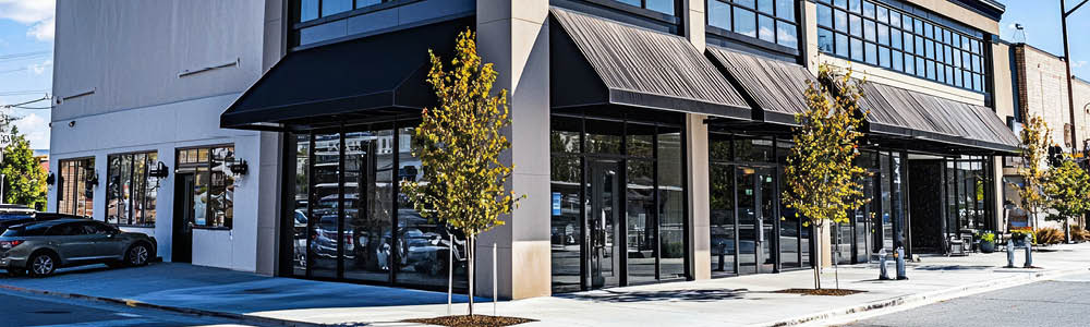 Image of a modern commercial building with large storefront windows, black awnings, and landscaping. Ideal for retail or office space.