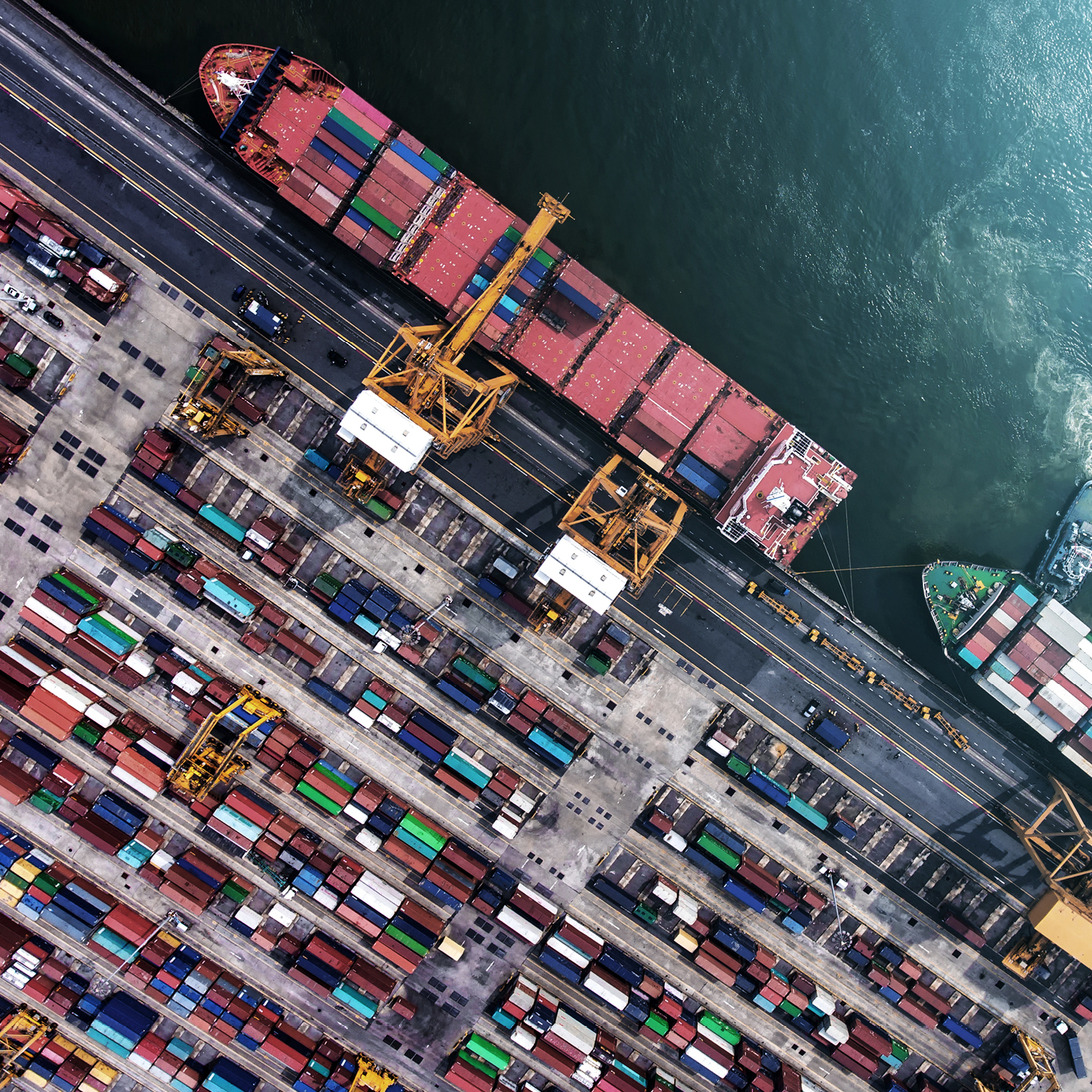 Aerial view of a busy cargo port with container ships and cranes loading and unloading shipping containers.