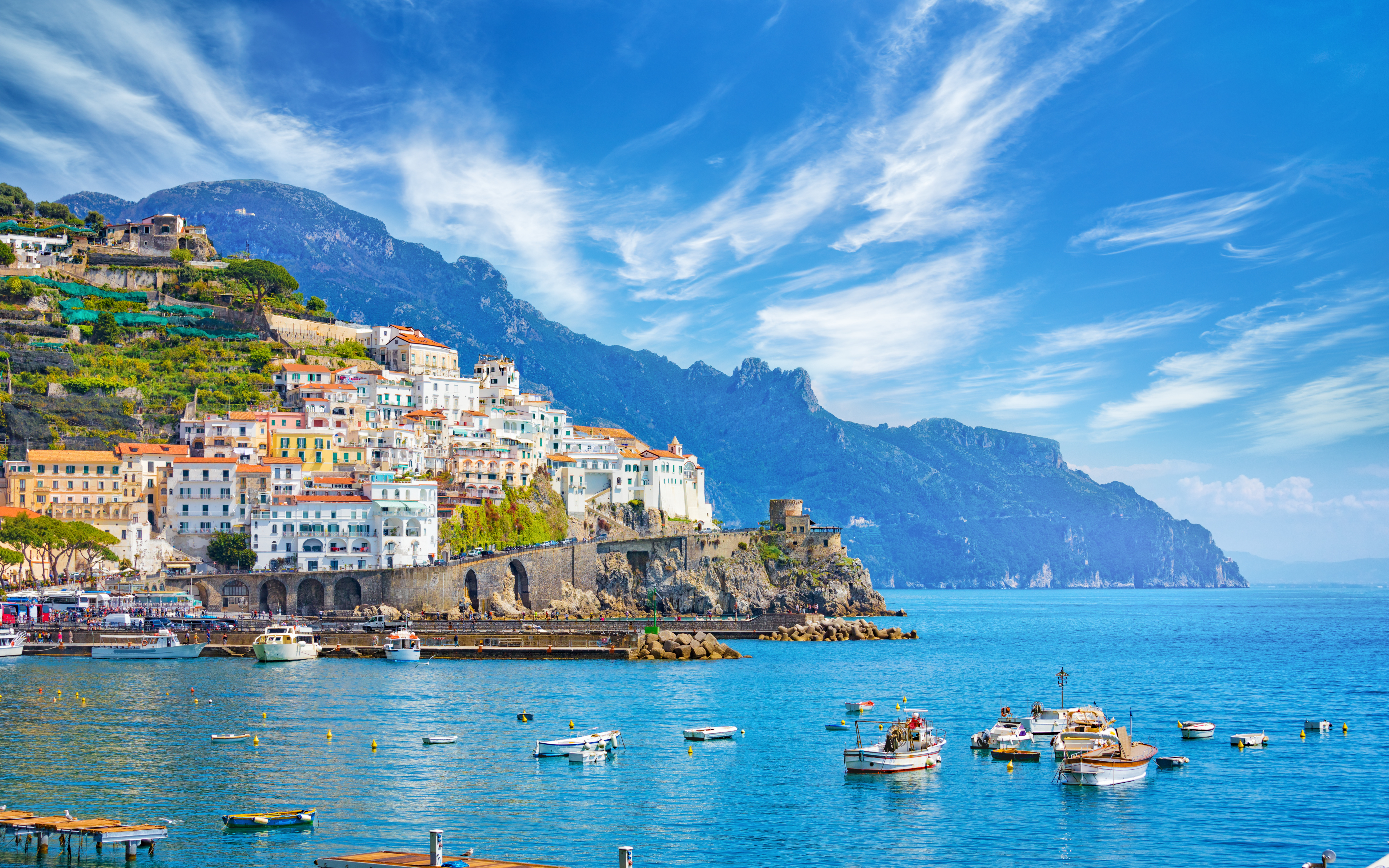 Sunny Amalfi Coast town, colorful buildings, boats in harbor.