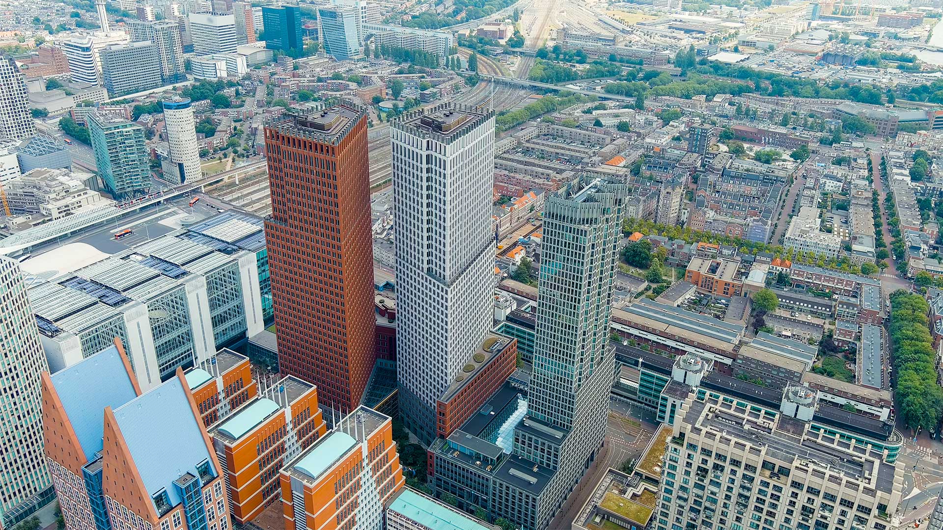Aerial view of a cityscape with a mix of modern and traditional architecture, with tall buildings in the foreground and a densely built-up area stretching into the distance.