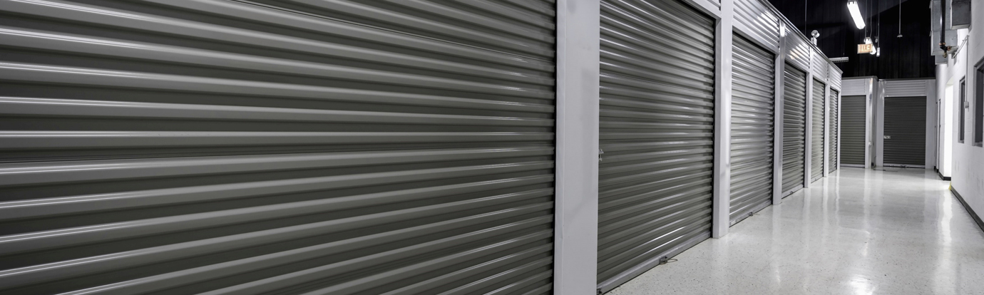 Row of closed, dark gray metal storage unit doors in a clean, well-lit hallway.