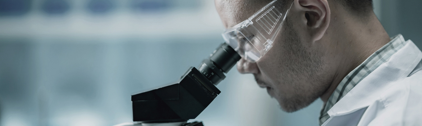 Close-up of a scientist wearing safety glasses, intently looking through a microscope in a laboratory setting.