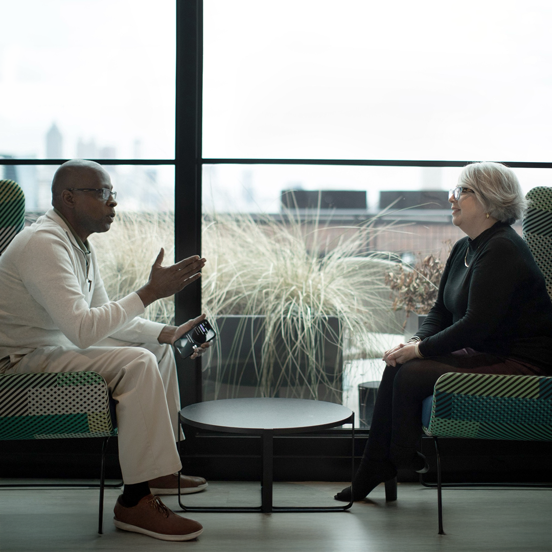 Image shows a professional business meeting between a man and woman discussing commercial real estate. A tablet is visible.