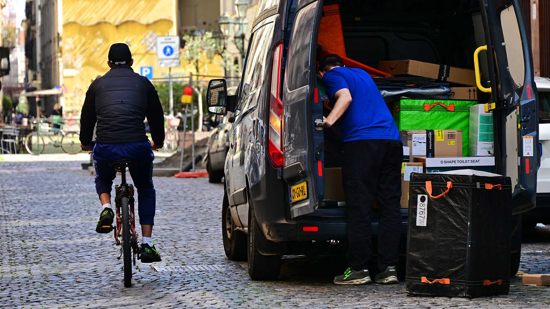 Image of an inner-city road where a van driver drops off a parcel as a cyclist passes by.