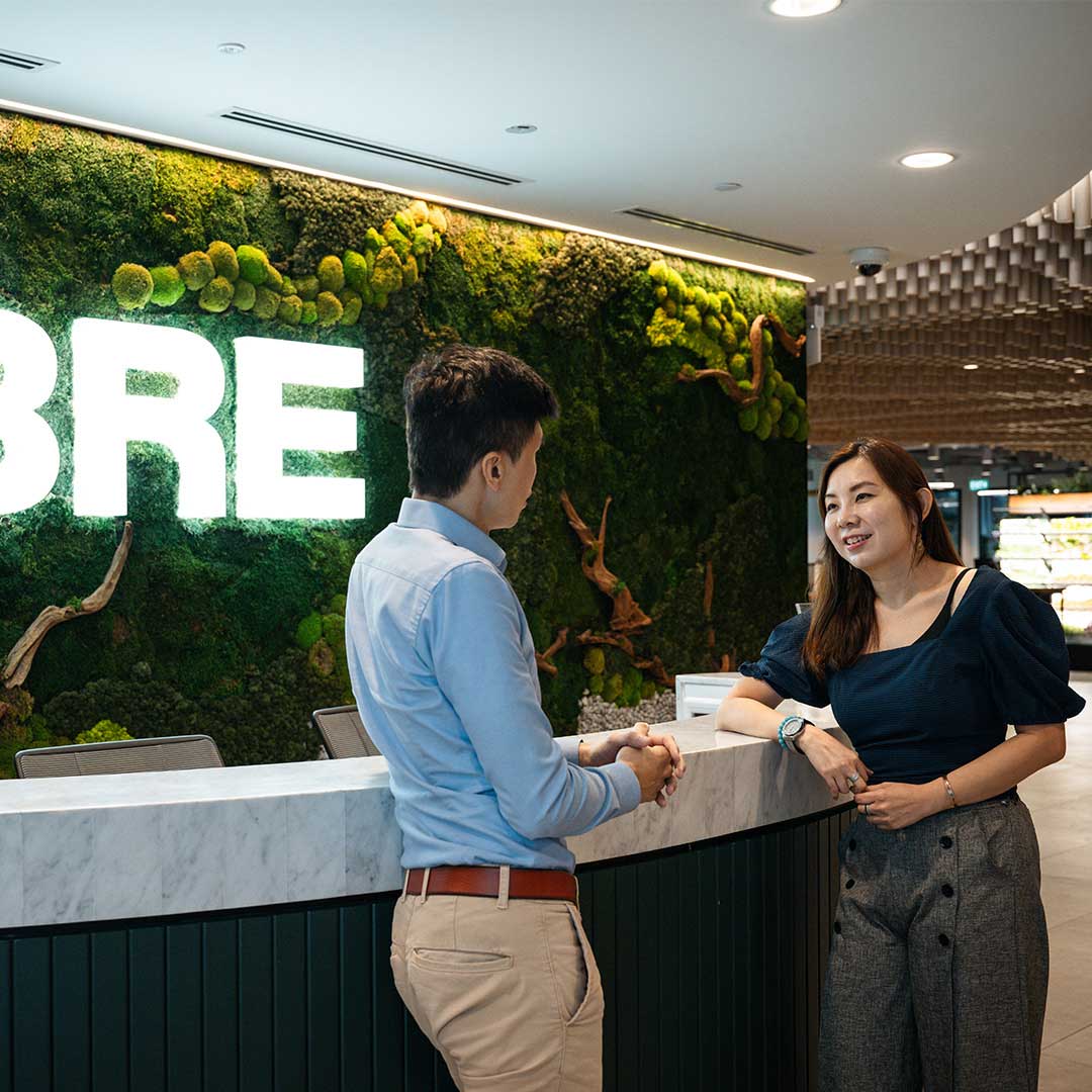 Man and woman in office talking at reception desk with greenery.