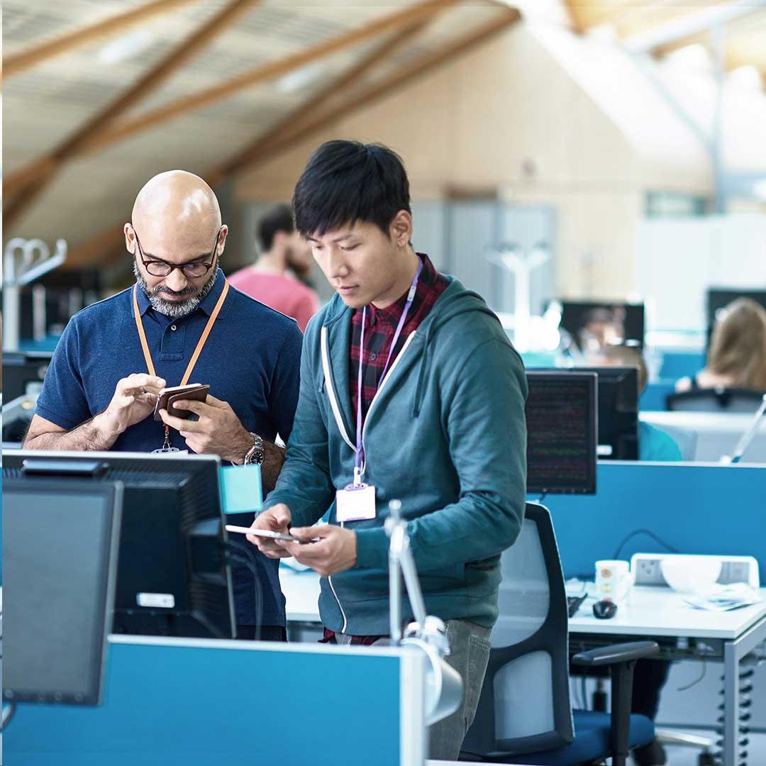 two employees looking at electronic devices in an office