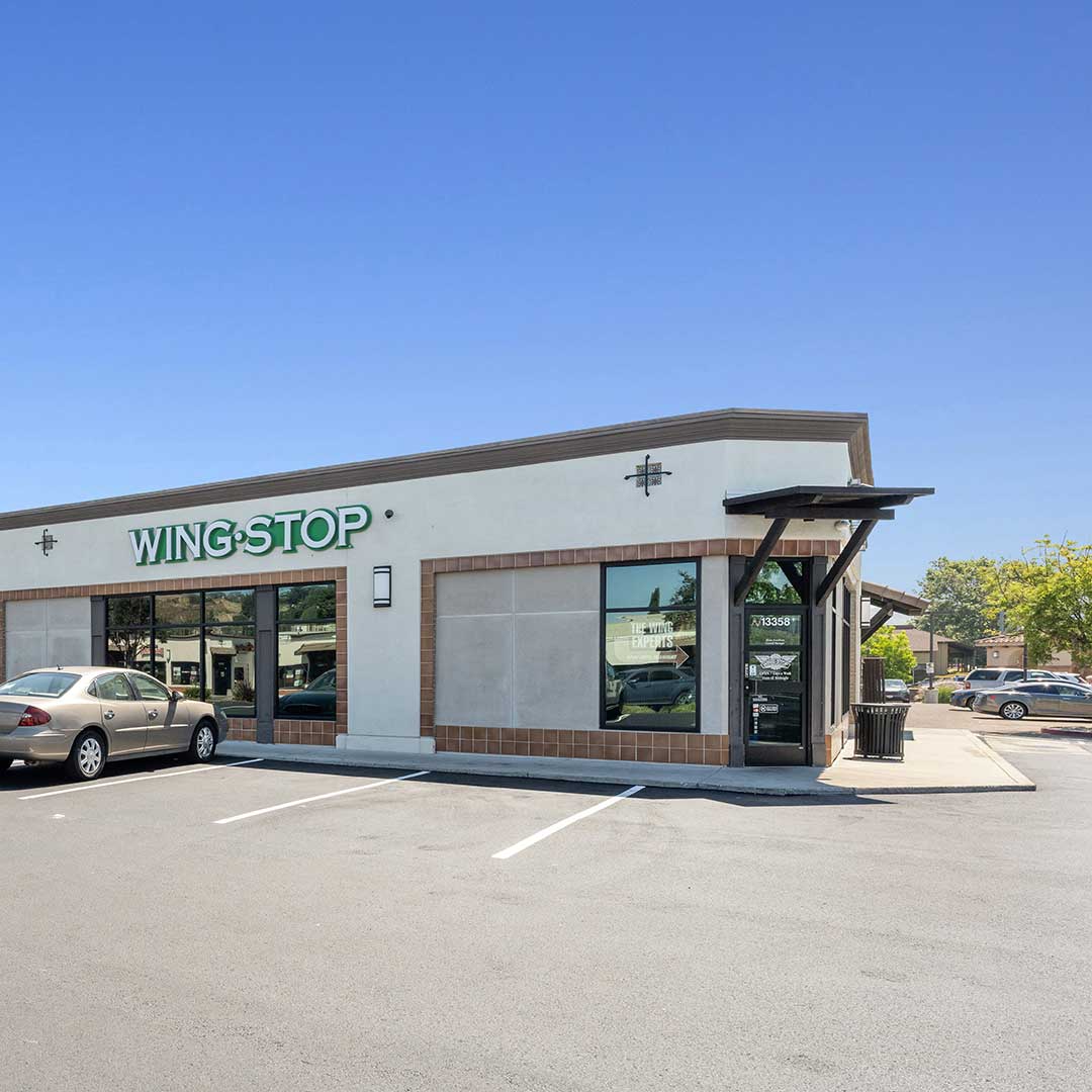 Front view of a wine shop featuring large windows, a welcoming entrance, and a variety of wine bottles displayed outside.