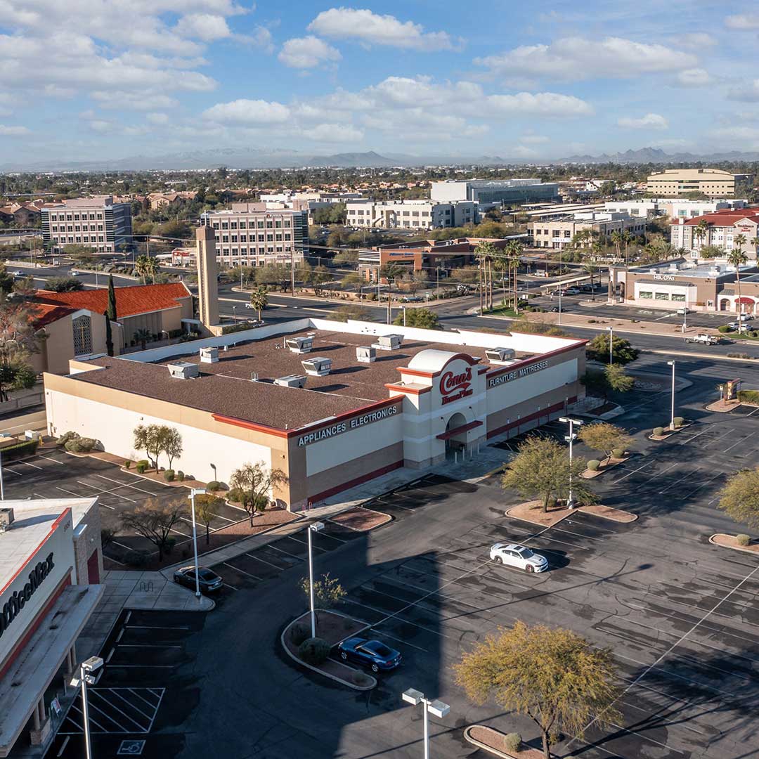 Aerial view of a parking lot adjacent to a building, showcasing parked vehicles and surrounding landscape.
